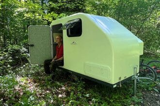 Caravan da bici compatta alpencamper eco slide out agganciata a una bicicletta